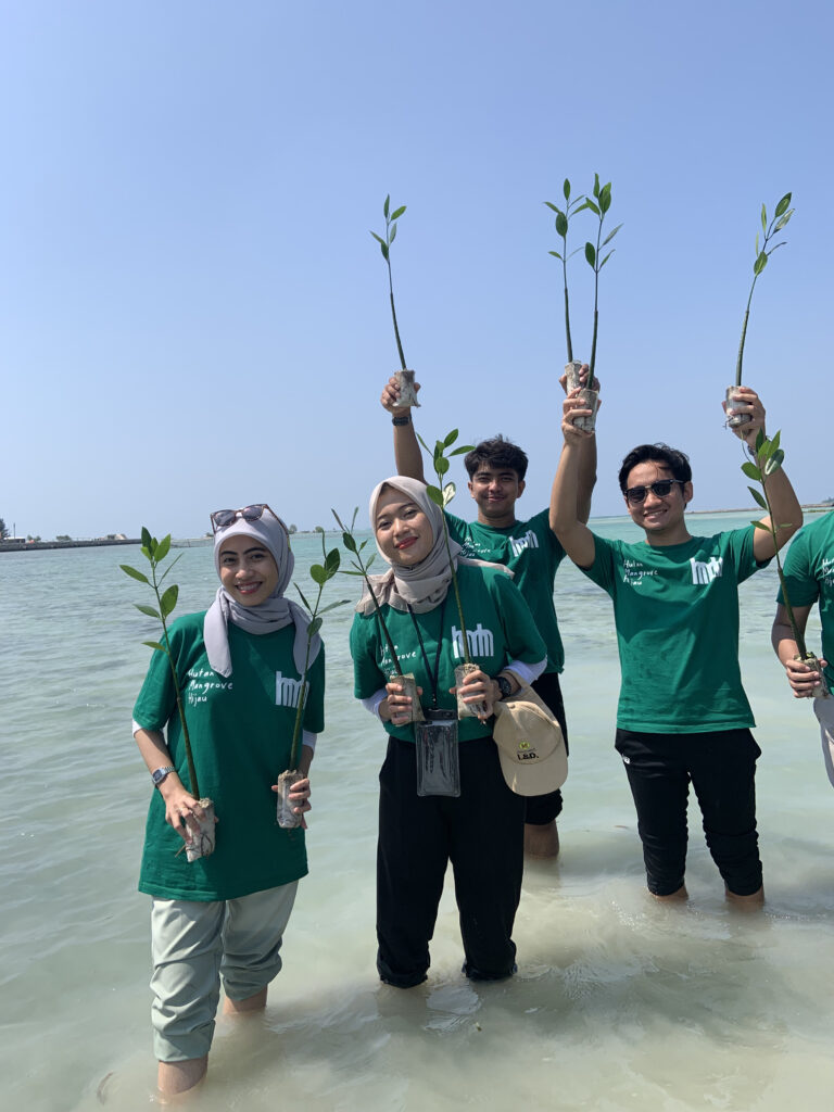 2 wanita dan 2 pria peserta gathering kantor dengan seragam kaos hijau Bumi Journey memegang benih-benih bakau pada kedua tangan mereka
