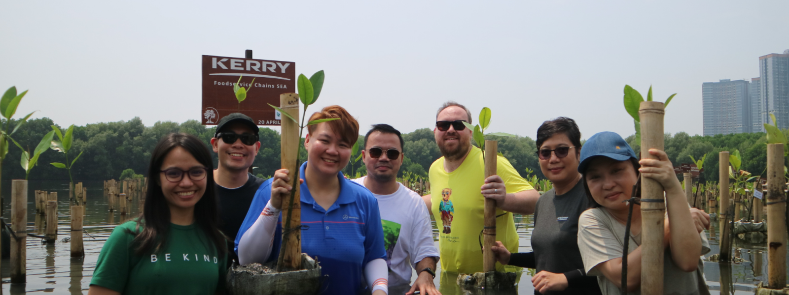 peserta acara penanaman mangrove dari perusahan Kerry berdiri di atas genangan air pantai area konservasi mangrove