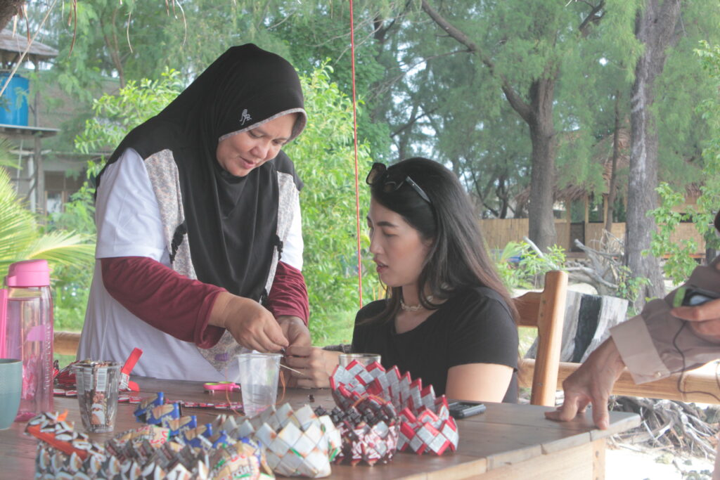 seorang ibu warga lokal mengajari peserta gathering kantor mengenyam souvenir dari bahan sustainable lokal