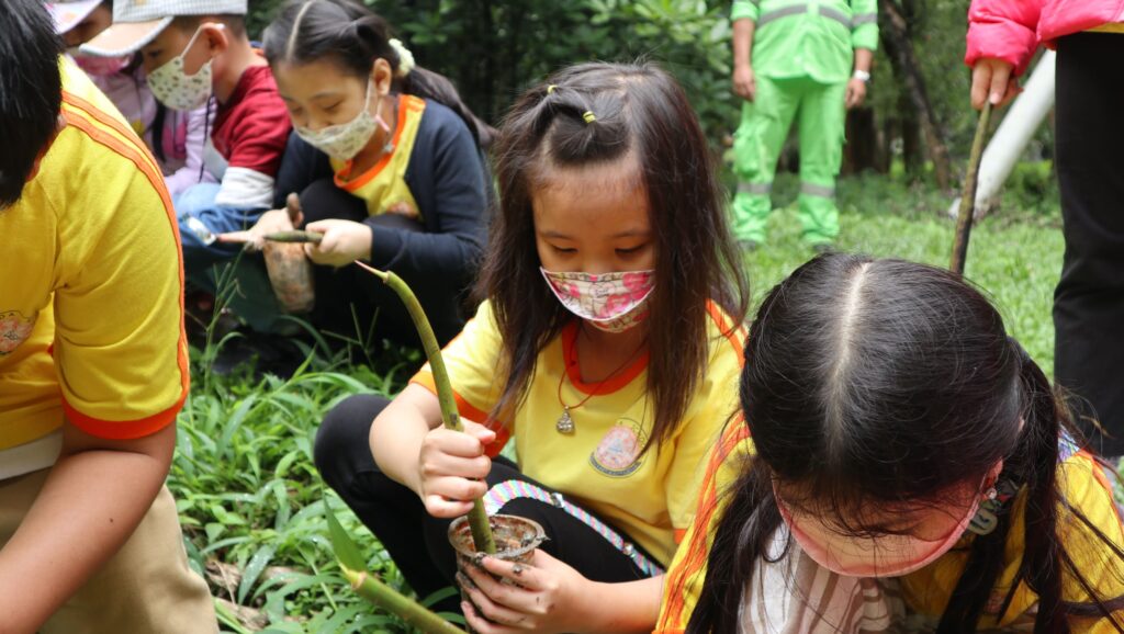 Anak-anak sekolah berseragam kuning dan masker memegang propagul mangrove dalam study tour Bumi Journey