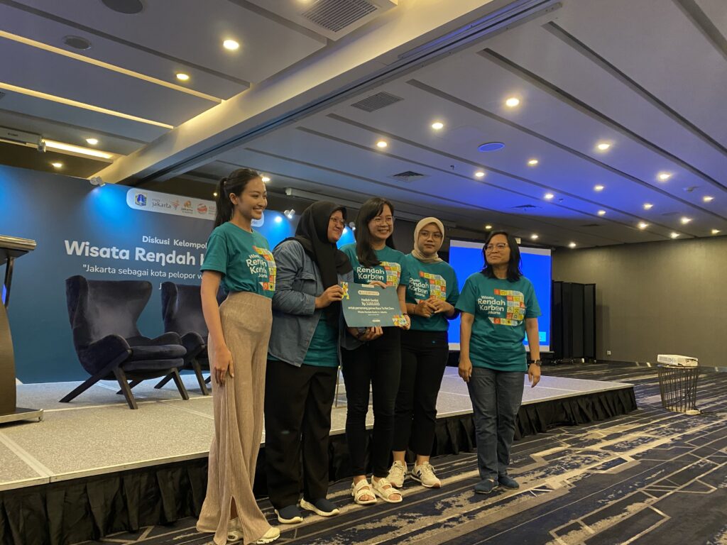 5 panelis acara Diskusi Kelompok Wisata Rendah Karbon berfoto di depang panggung sambil memegang kertas sertifikat semacam penghargaan