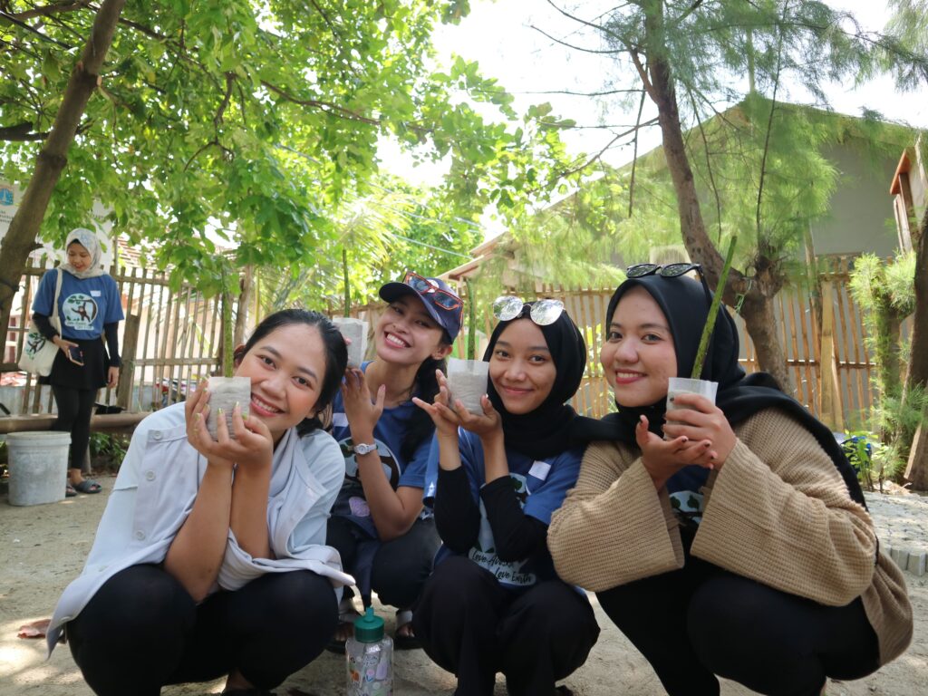 4 orang wanita cantik peserta mangrove planting trip Bumi Journey berjongkok di lokasi nursery bibit mangrove sambil memegang bibit mangrove.